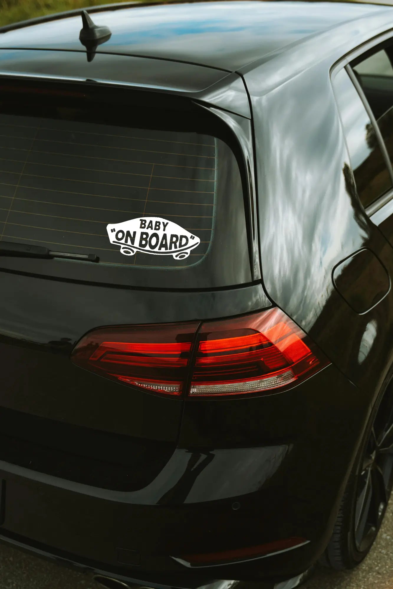 Baby on board gördeszka matrica fehér színben az autó hátsó ablakán.