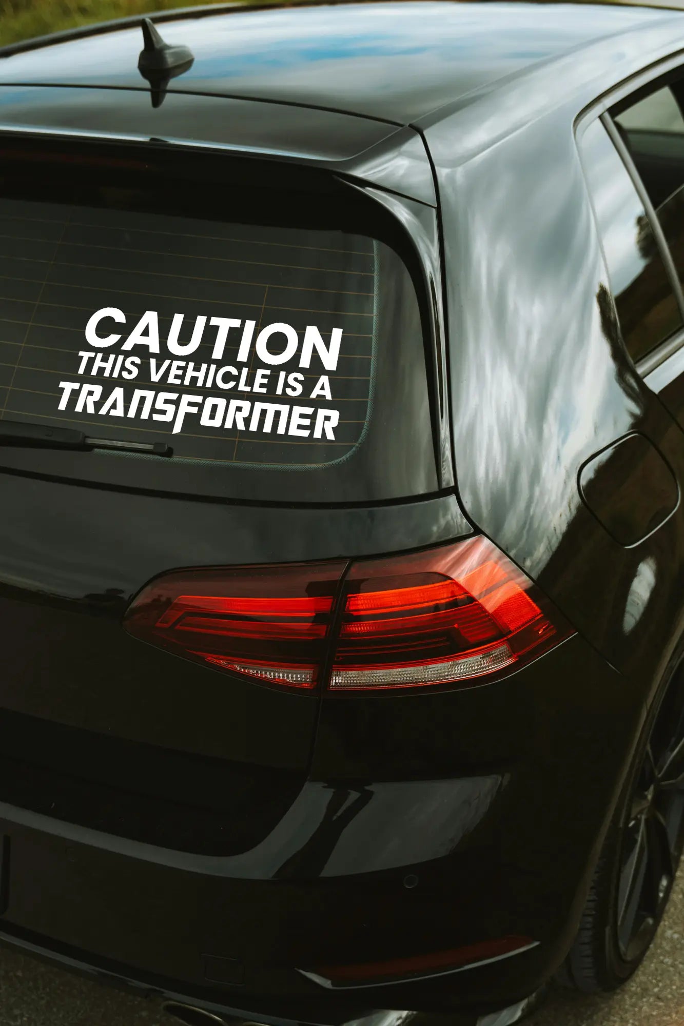 CAUTION This vehicle is a TRANFSORMER matrica fehér színben az autó hátsó ablakán.