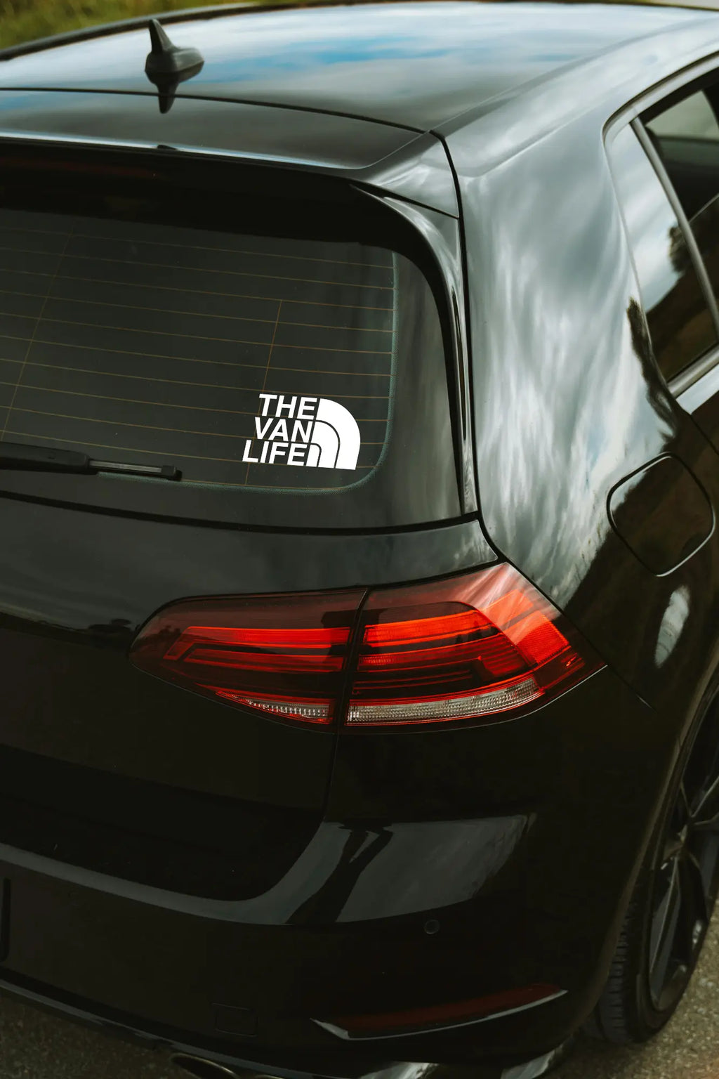 The Van Life matrica fehér színben az autó hátsó ablakán.